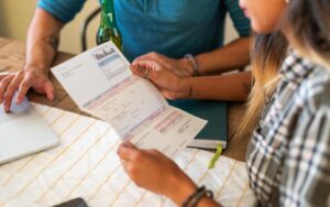 Two people sitting at table with a laptop and notebook to plan how to manage their bills.