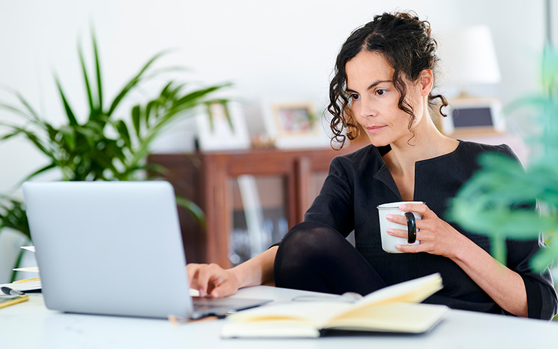Woman holding coffee cup working on budget on computer