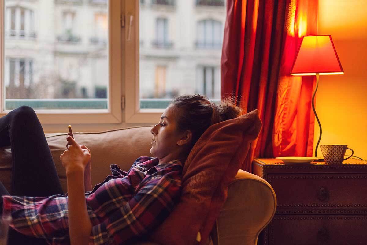 woman browsing phone while laying on couch at home