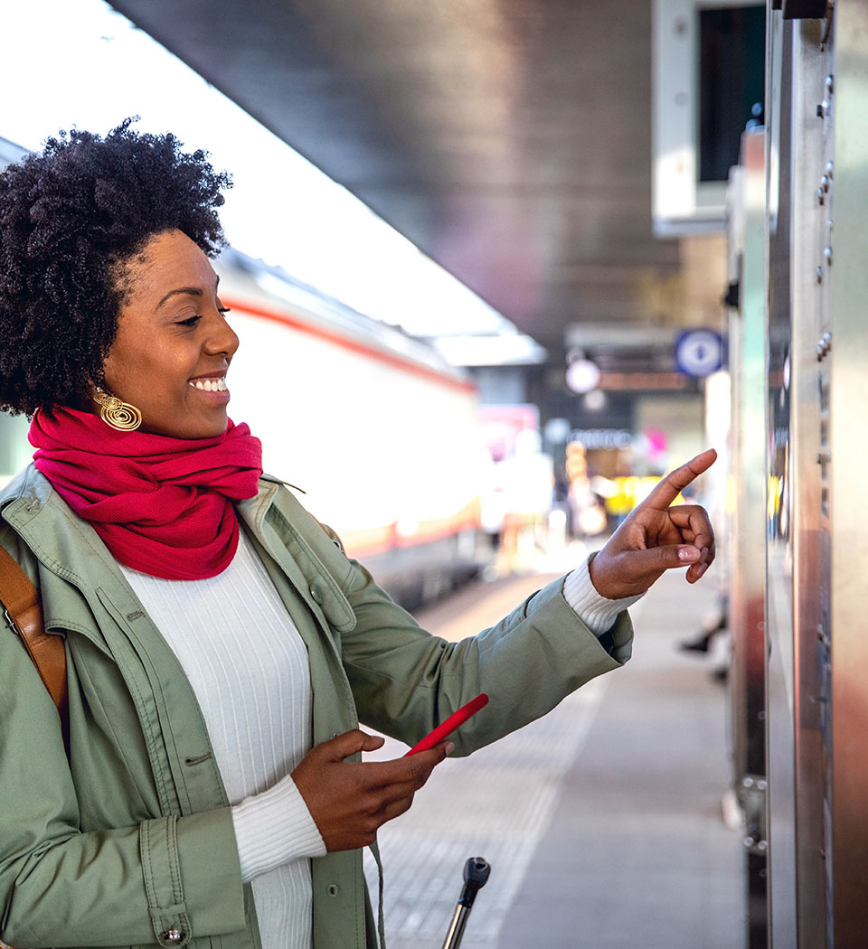 Smiling woman with phone at station points at train schedule