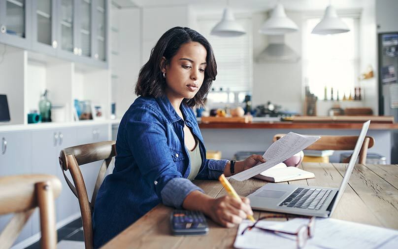 Woman working through paperwork at her desk with laptop