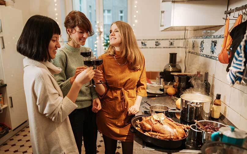 Family and friends standing around the oven making Thanksgiving dinner