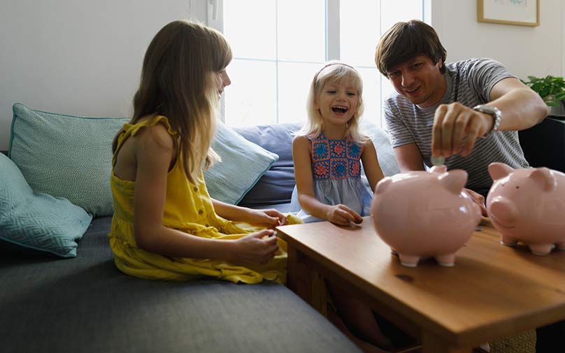 Father sitting with daughters putting money in a piggy bank