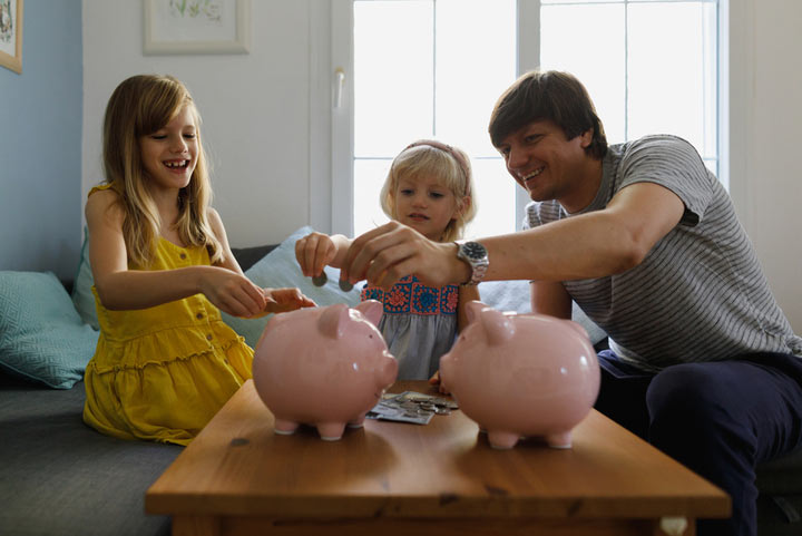 Father and two young daughters putting money into piggy bank