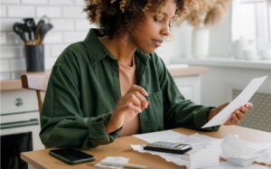 Woman in her kitchen sorting and figuring out how to budget using a calculator.