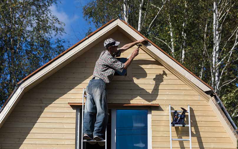 Man standing on ladder paints trim on outside of home