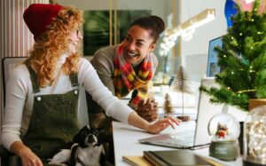 Two women smiling at each other surrounded by holiday decor cyber Monday shopping