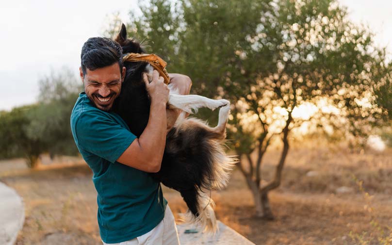 Man standing outside, happily hugging his dog