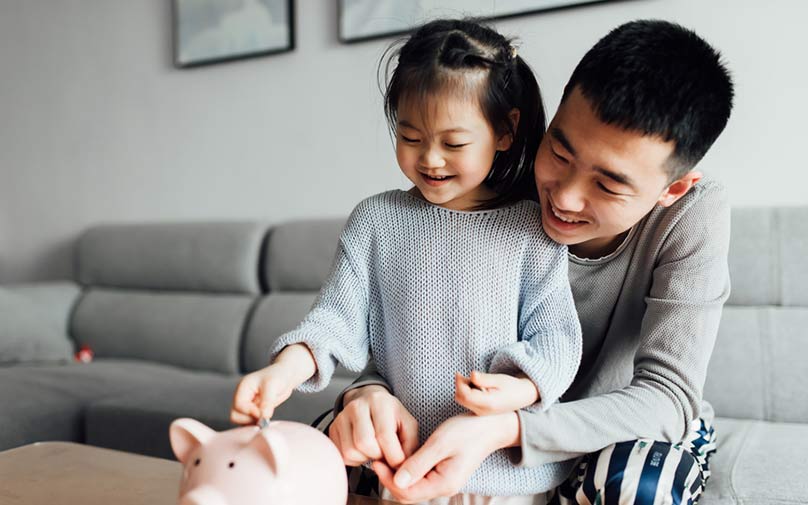 Father teaching daughter how to save, helping put coins in piggy bank