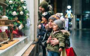Family of four in winter clothes holiday shopping looking through a department store window with Christmas items.