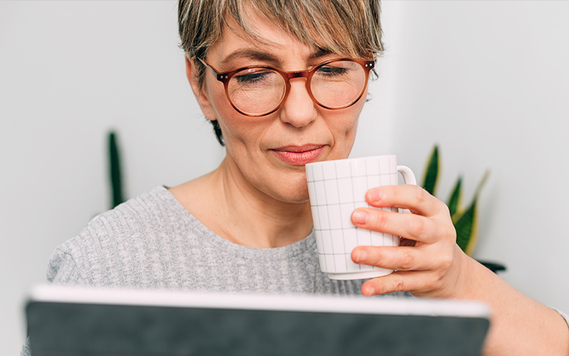 Woman drinking coffee while looking at laptop