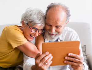 Happy senior couple laughing while using tablet together on living room sofa